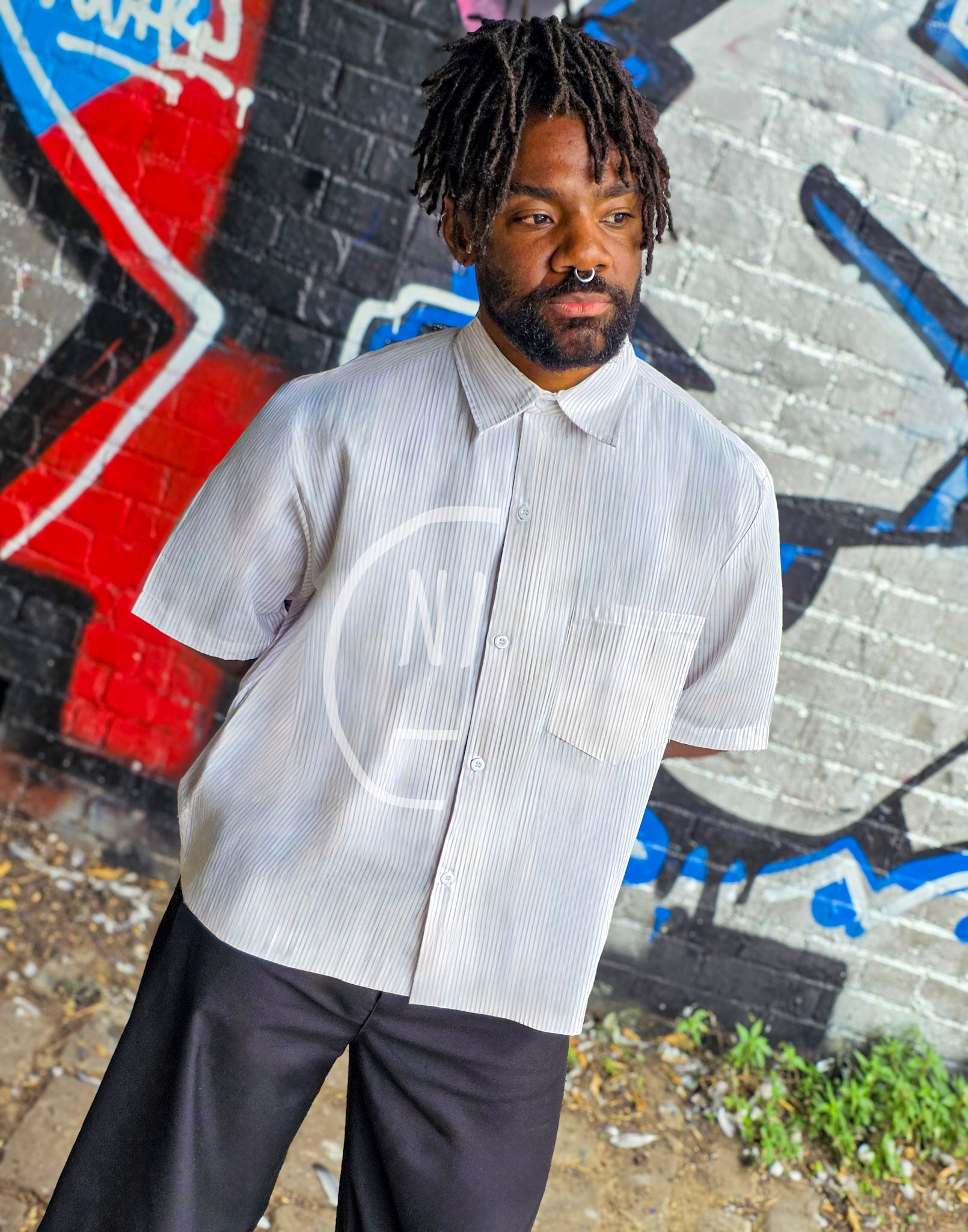 Person wearing a white shirt with a logo in front of a graffiti-covered wall.