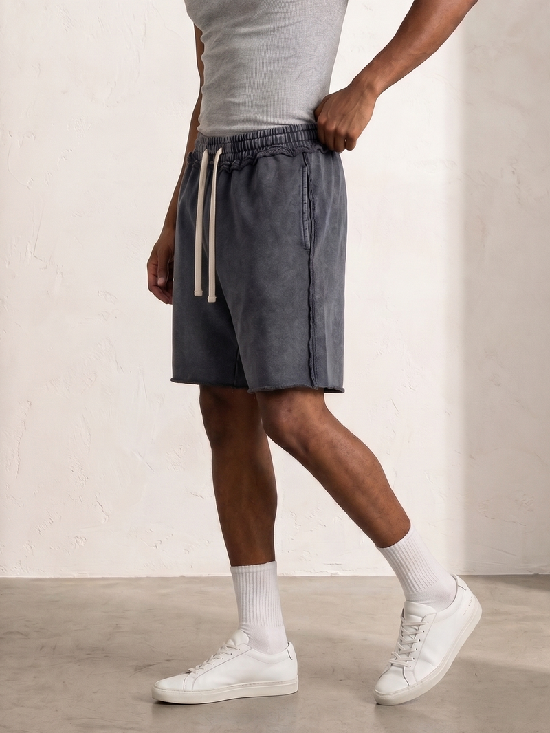 Person wearing gray shorts with white drawstrings, white socks, and white sneakers against a plain background