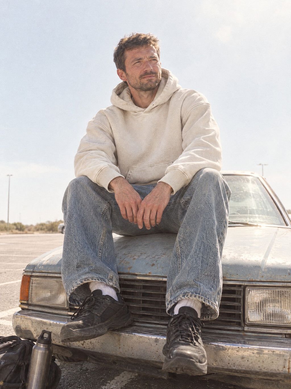 Man wearing the Snow Wash Oversized Hoodie in Mild Apricot, sitting on a vintage car